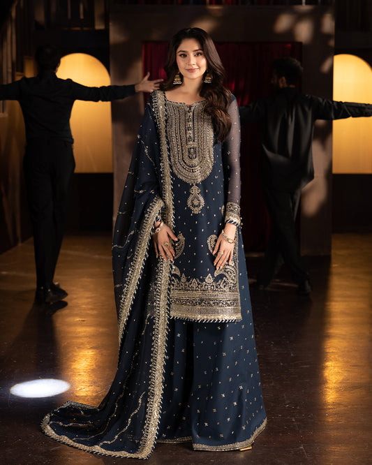 Front view of navy blue embroidered sharara set with gold sequins, sheer sleeves, and flowing dupatta.