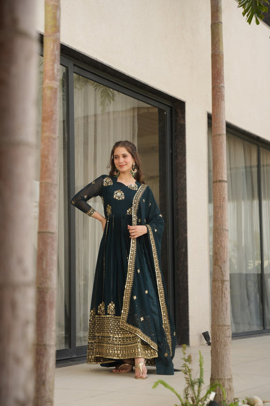 Woman in Rama green designer gown with dupatta, standing outdoors.