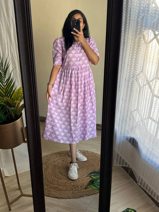 Reflection of a woman in a lilac Ghibli Maxi dress with a white floral pattern and white sneakers.