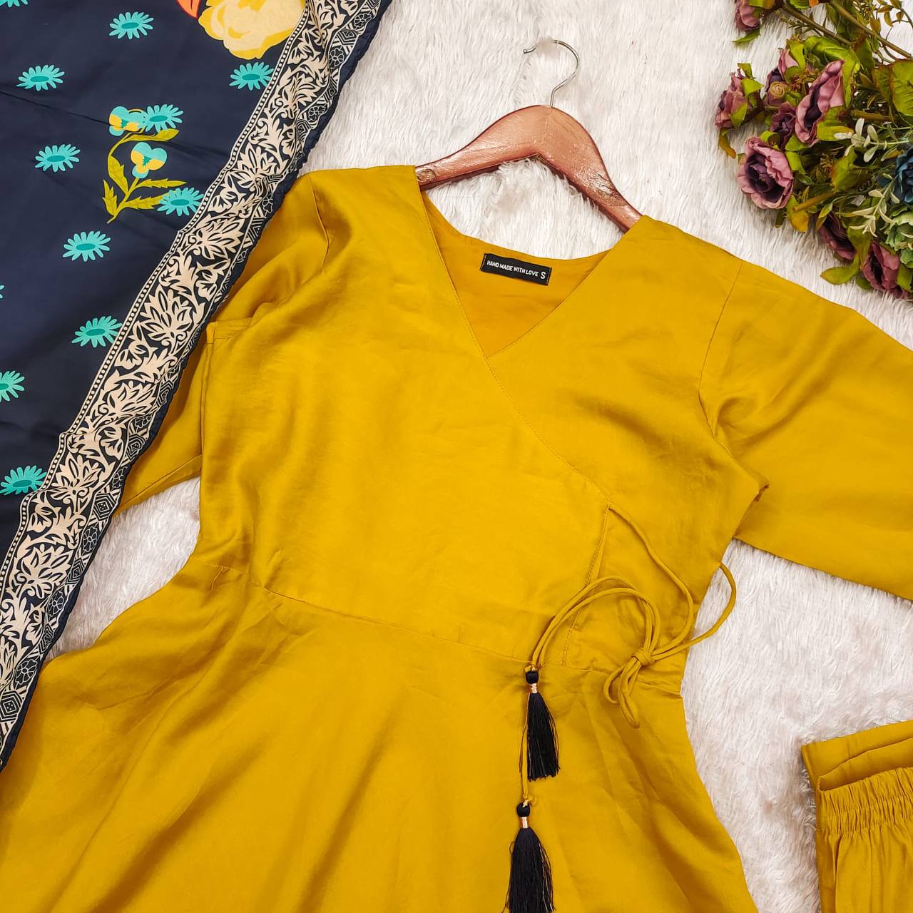 Close view of yellow suit set’s wrap top, black tassels, and navy blue floral dupatta.