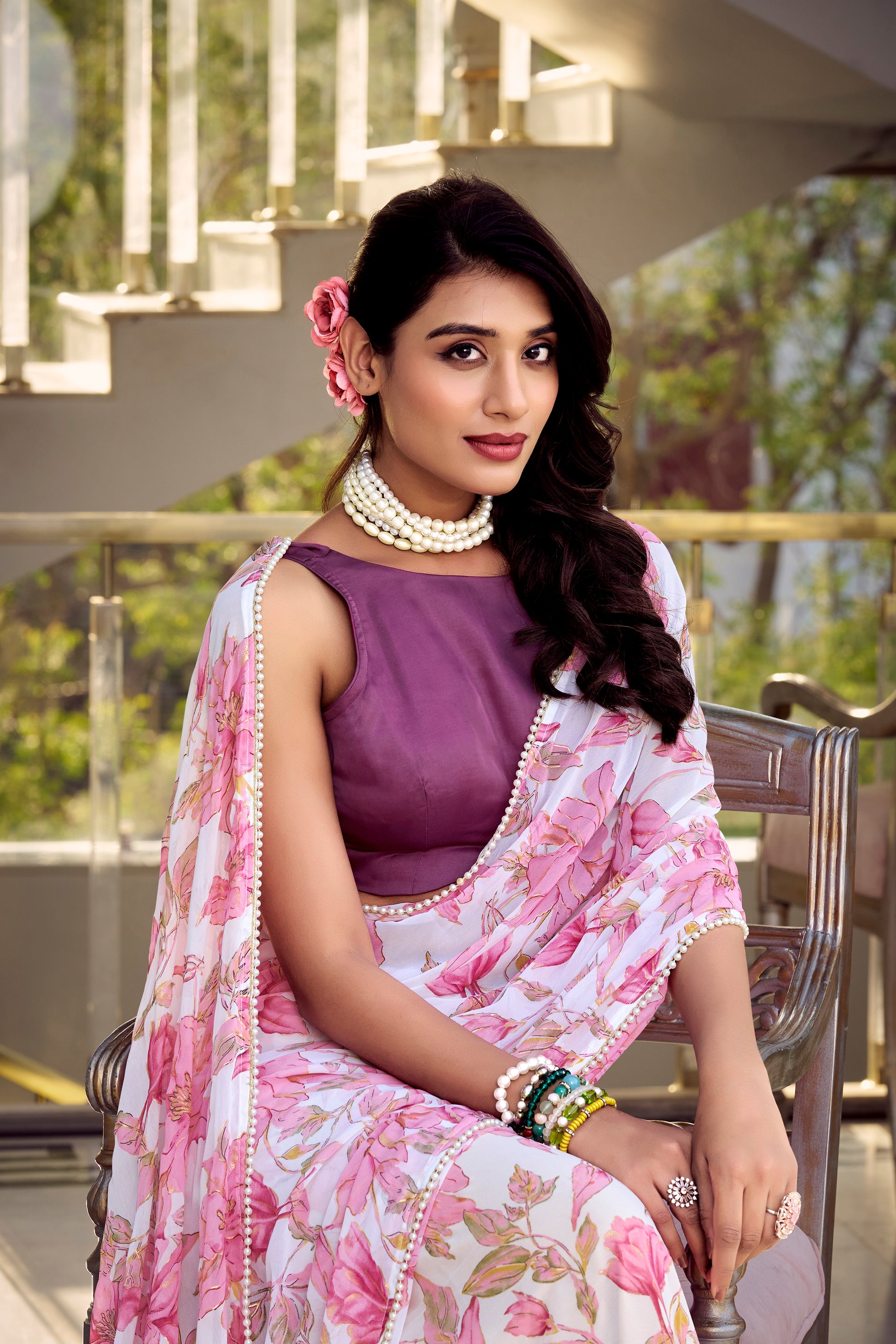 Model seated, wearing a lilac pink floral print saree with pearl necklace.