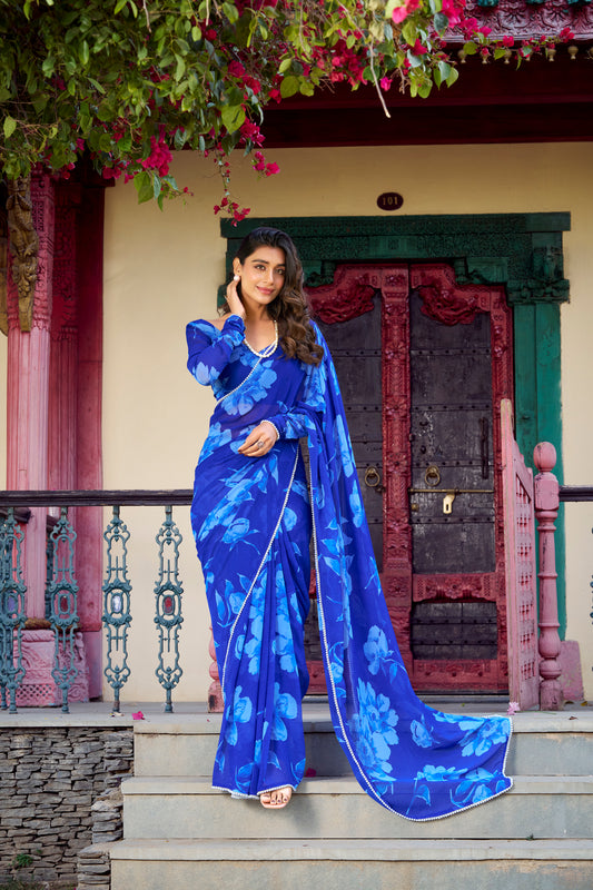 Elegant woman posing in a light blue floral Indian saree with pearl jewelry.