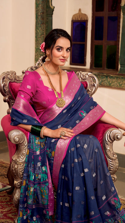Model sitting in chair wearing navy and pink silk saree with jewelry.