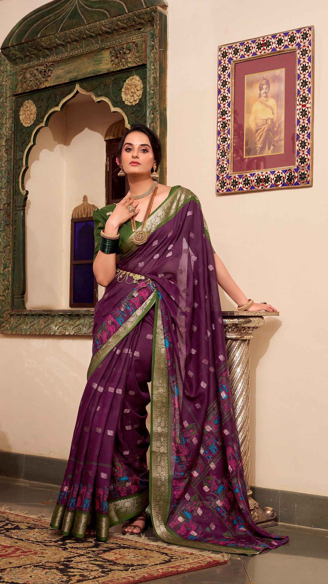 Elegant woman in a plum saree with zari border and green blouse.