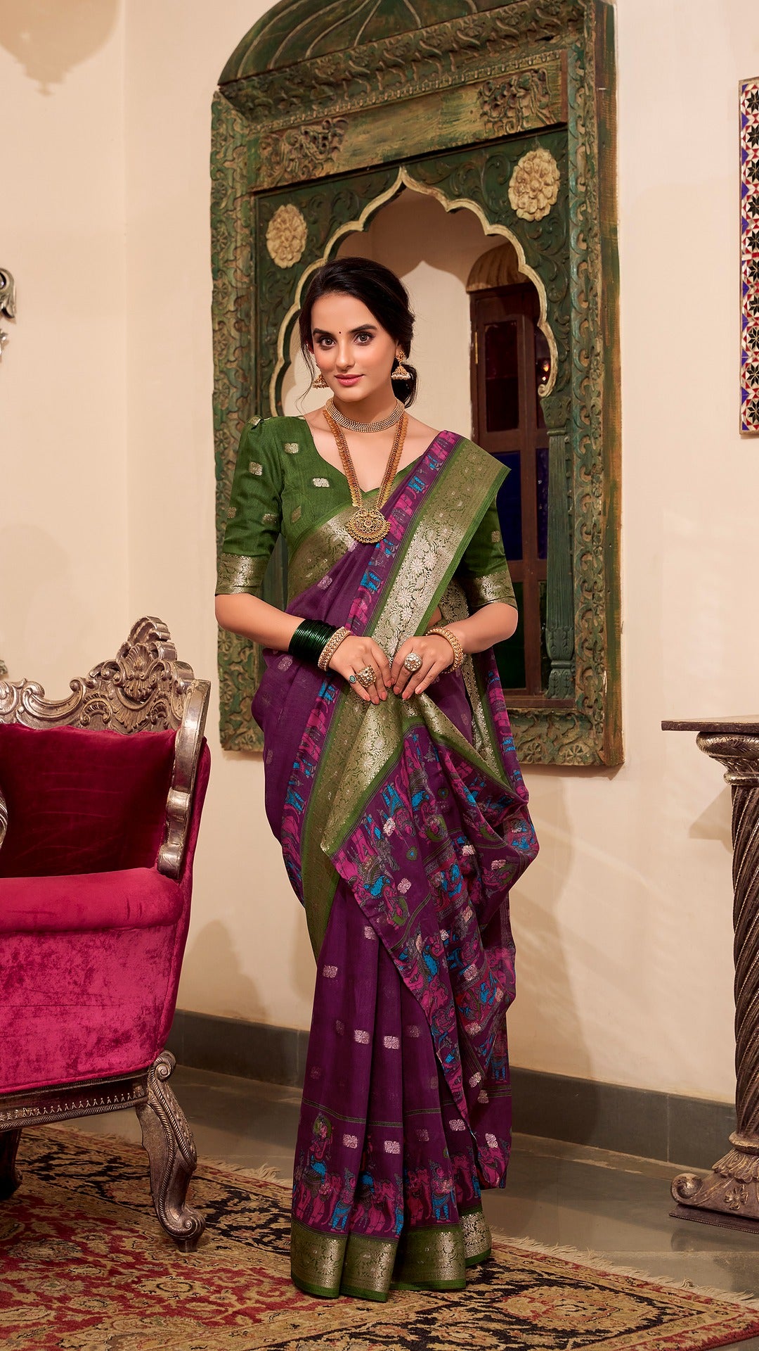 Full view of model in plum saree with green blouse and gold jewelry.