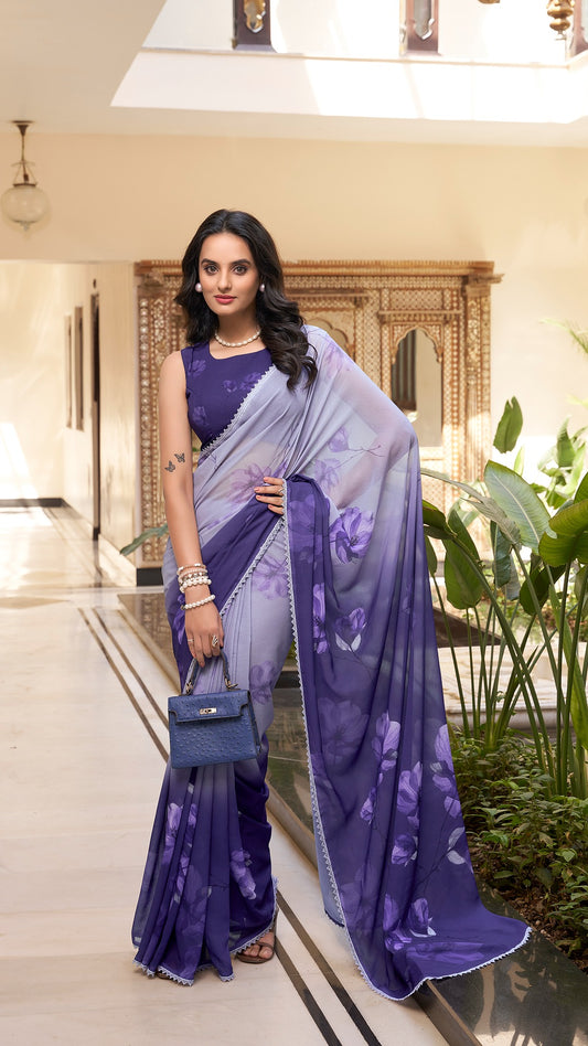Woman in a stylish purple floral saree holding a blue handbag.