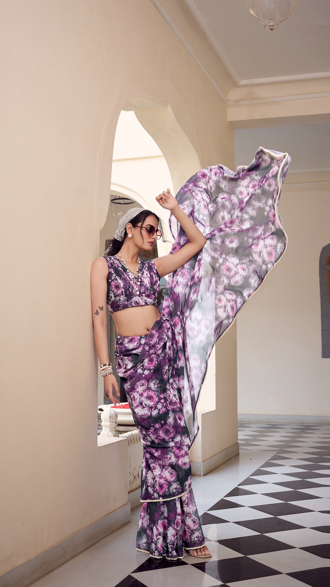 Model poses in purple floral saree with sunglasses in a windy setting.