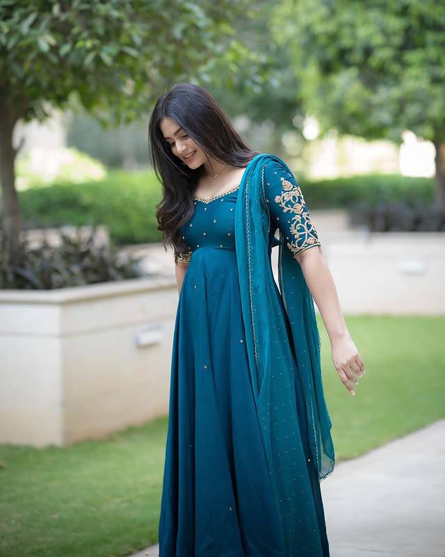 Model in teal embroidered Morpankh Anarkali with dupatta, standing in garden.