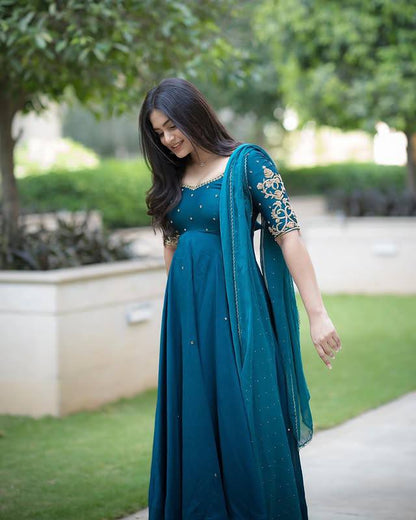 Model in teal embroidered Morpankh Anarkali with dupatta, standing in garden.