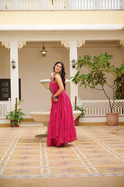 Woman posing in vibrant pink Bandhani Gamathi work gown with flared skirt and mirror work.