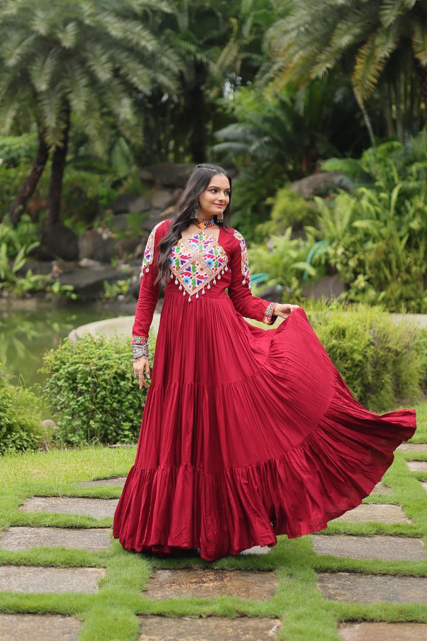 Woman holding maroon flared skirt of Kutchi embroidered Gamthi Gown, highlighting vibrant partywear design.