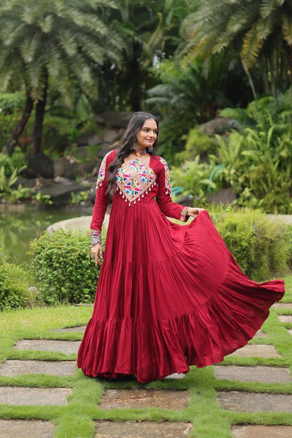 Woman holding maroon flared skirt of Kutchi embroidered Gamthi Gown, highlighting vibrant partywear design.