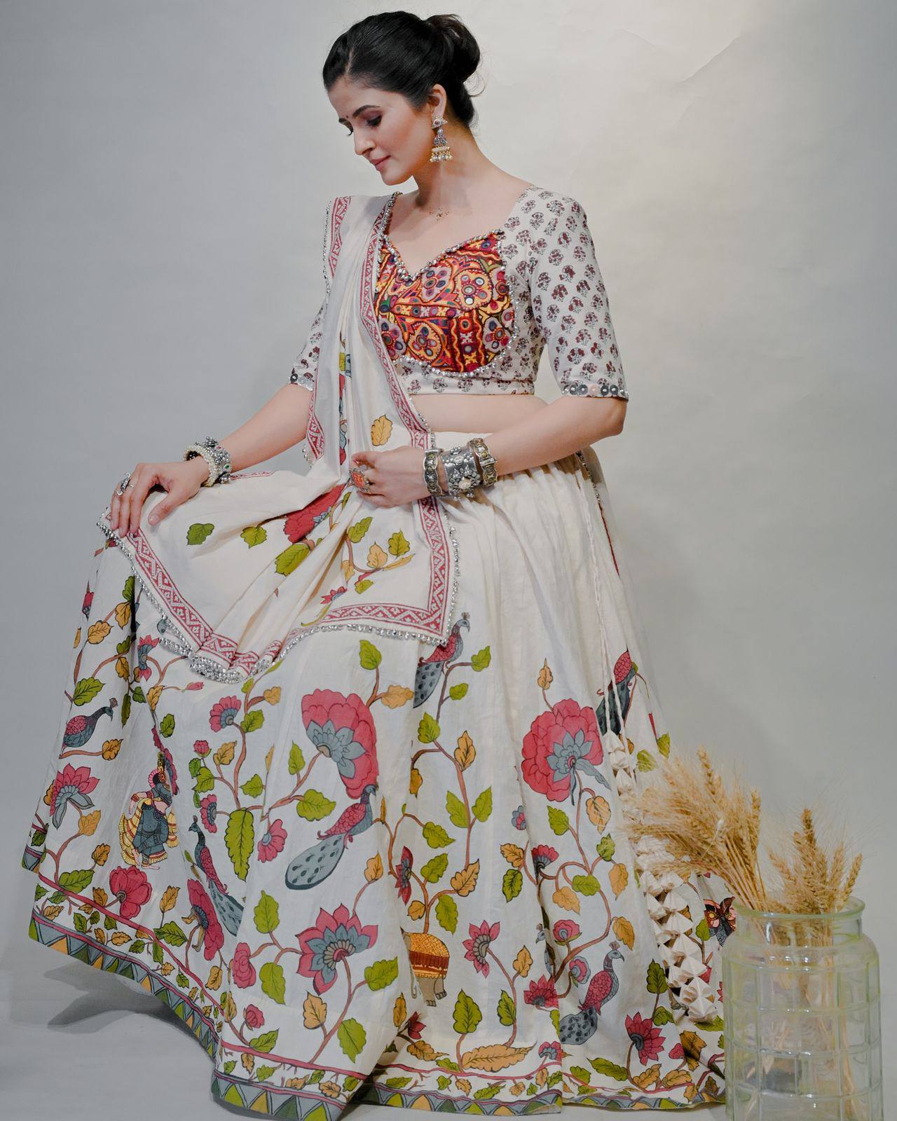 Seated woman in ivory cotton lehenga choli, vibrant mirror-embroidered blouse, and folk print skirt for Navratri.