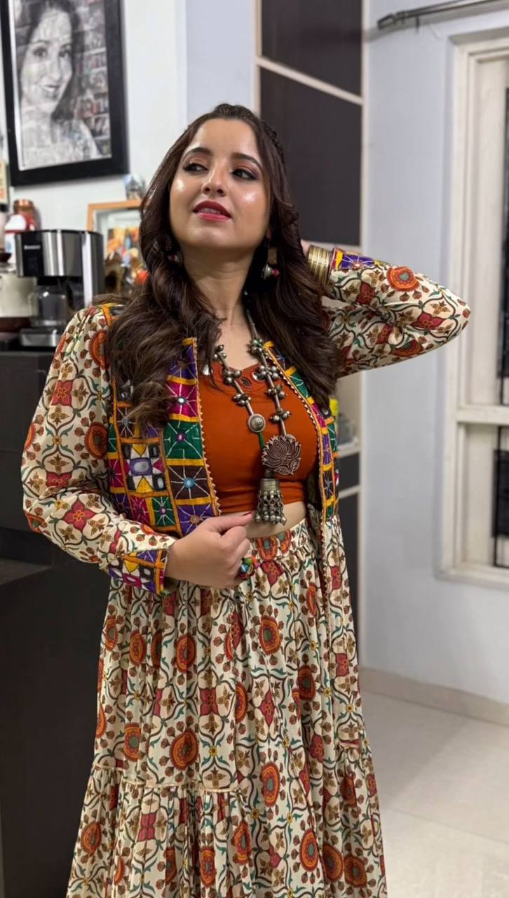 Close-up of festive lehenga choli set showing orange blouse, mirror work shrug, and floral embroidered skirt.
