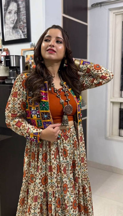 Close-up of festive lehenga choli set showing orange blouse, mirror work shrug, and floral embroidered skirt.