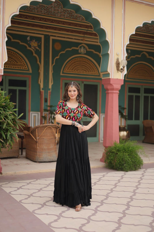 Woman in black Kutchi embroidered Navratri gown, standing outdoors, showing colorful bodice and maxi skirt.