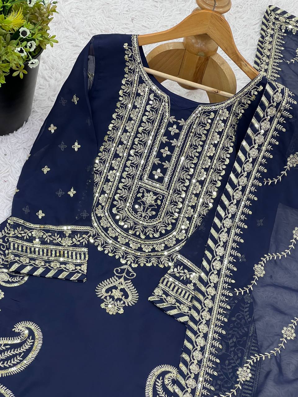 Detailed view of navy blue kurta’s gold threadwork and sequin embroidery, with dupatta on hanger.
