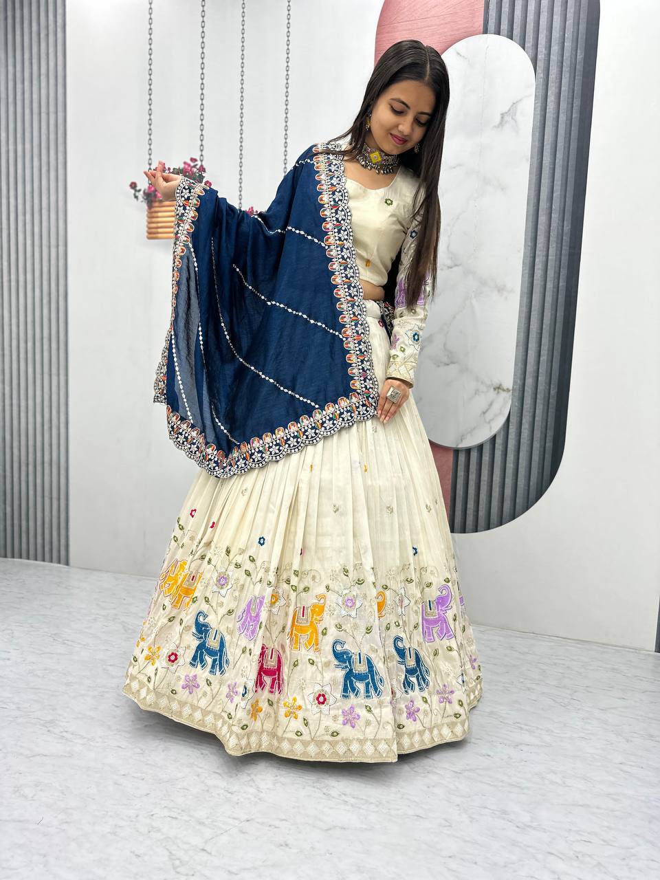 Woman in off-white lehenga choli with colorful elephant embroidery and a navy blue dupatta.