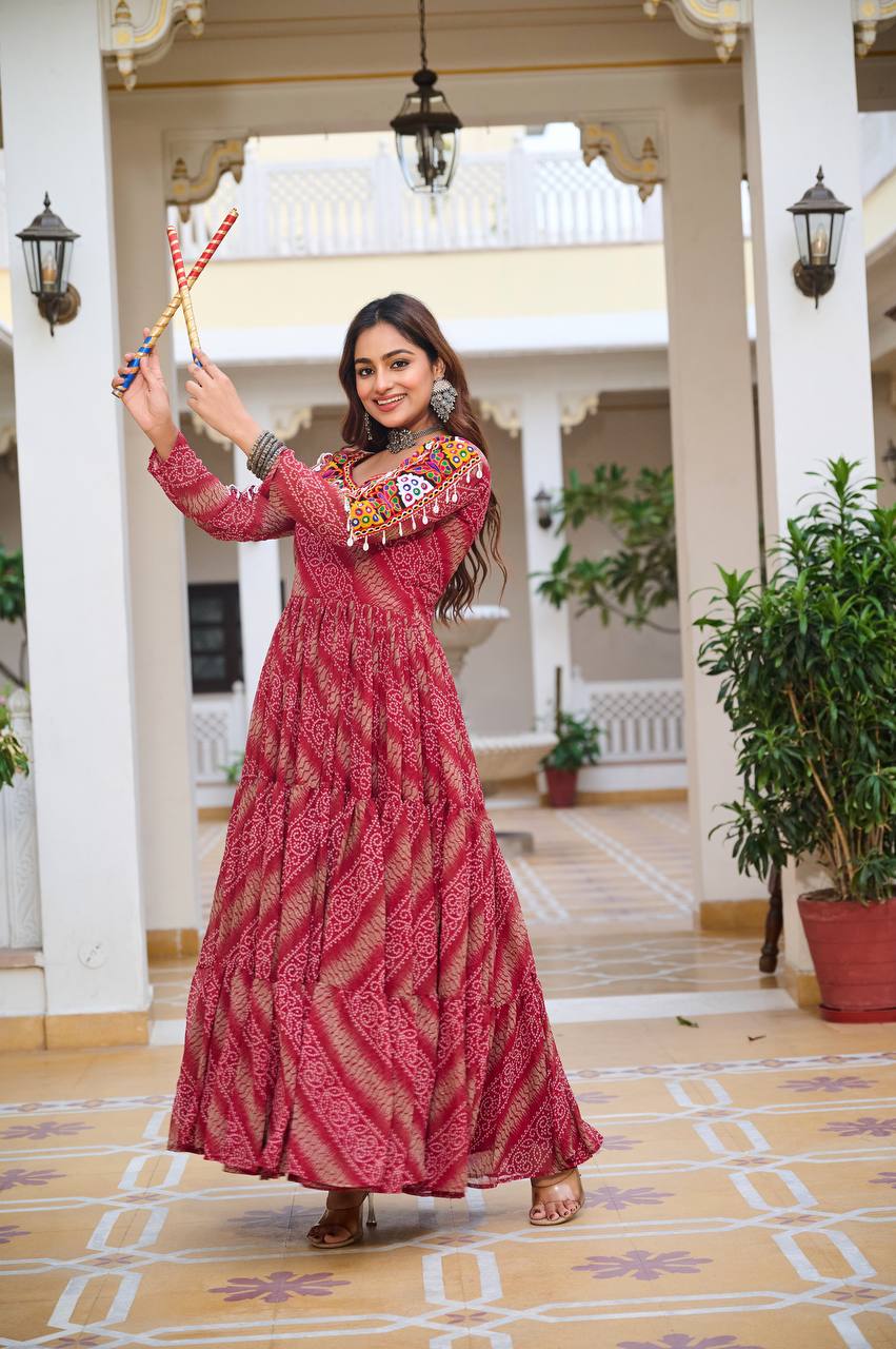 Woman in a red Bandhni print Gamathi work gown, posing with dandiya sticks, perfect for Navratri celebrations.