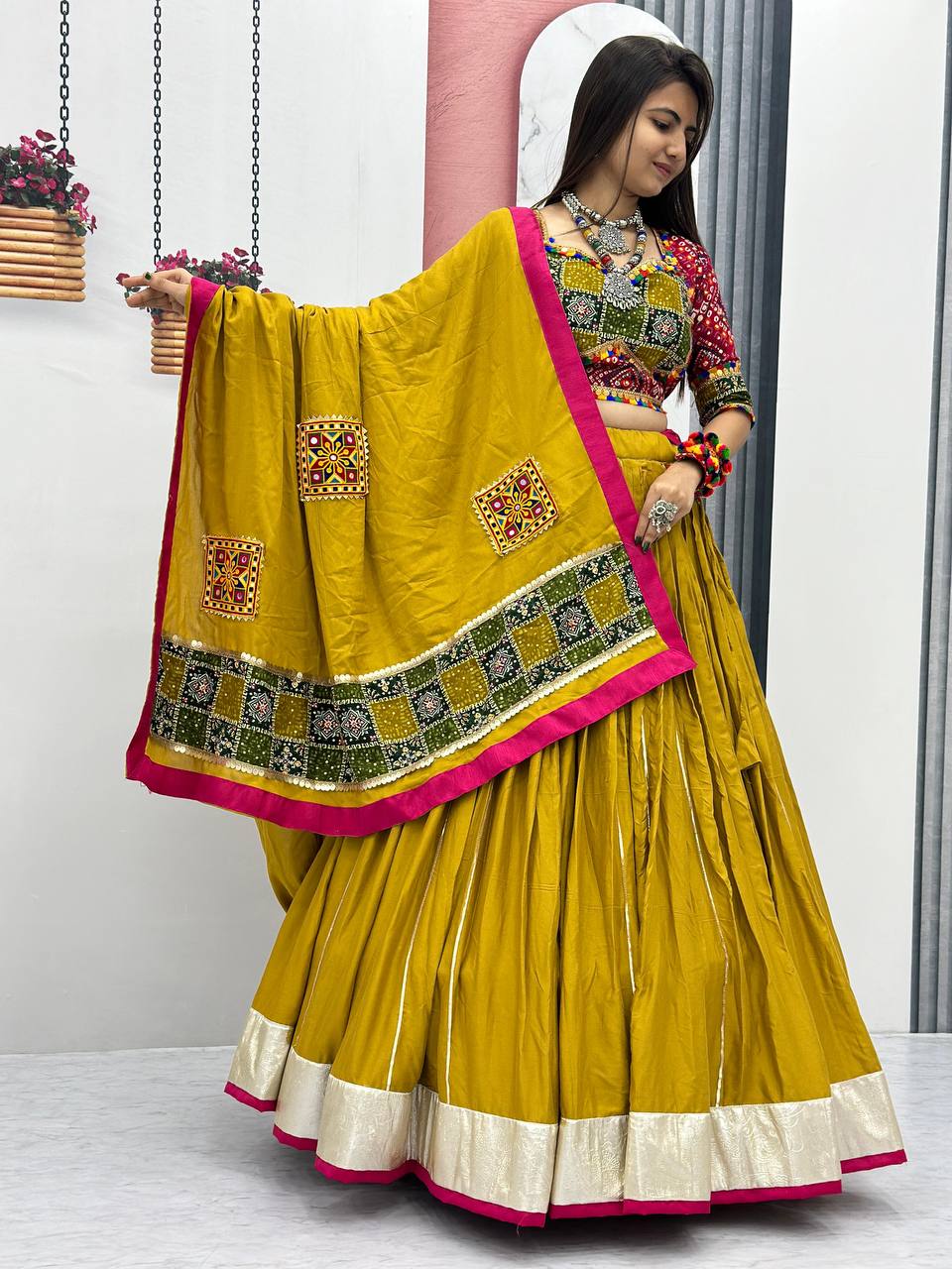 Woman showcasing mustard cotton lehenga with flared bottom and pink and gold dupatta.