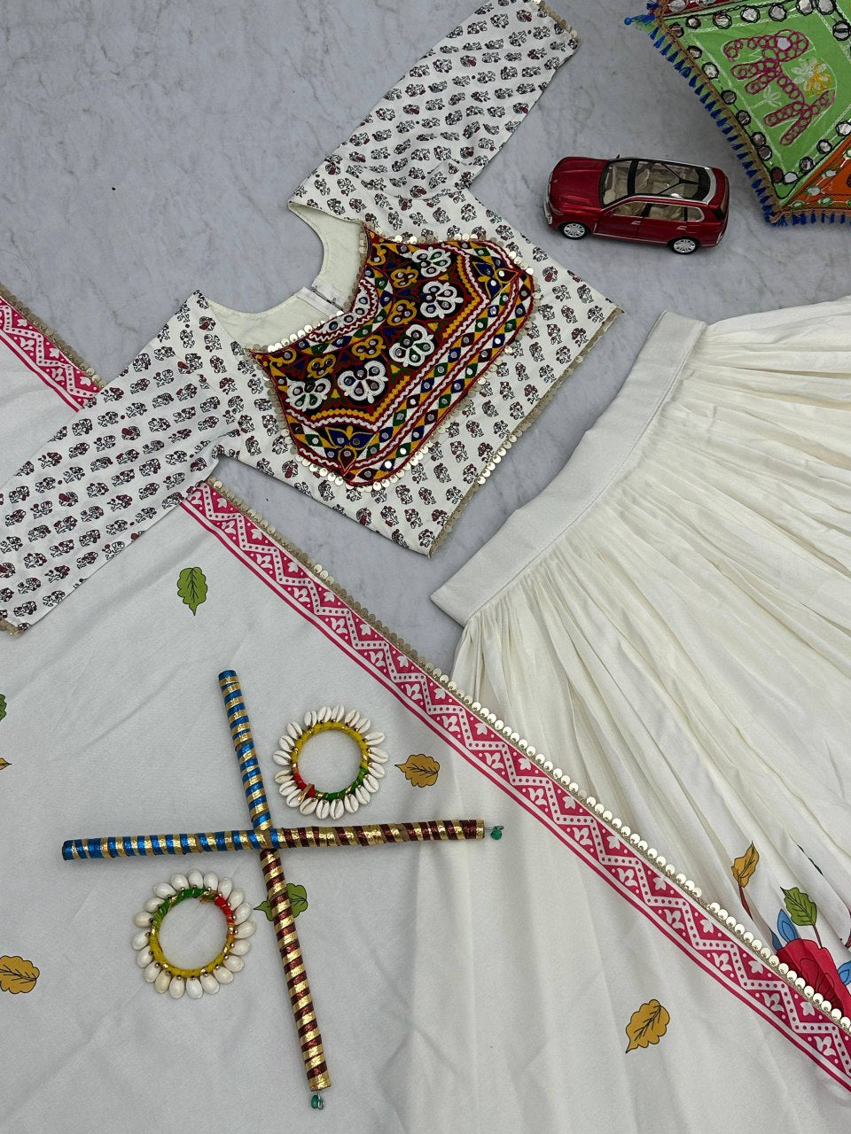 Flat lay of Gamthi Grace Lehenga Choli set with embroidered blouse, skirt, dupatta, bangles, and dandiya sticks.