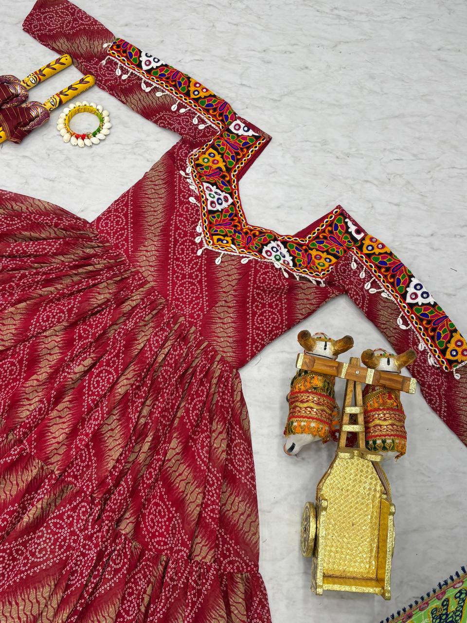 Close-up of red Bandhni gown's embroidered neckline, with dandiya sticks and traditional decor.