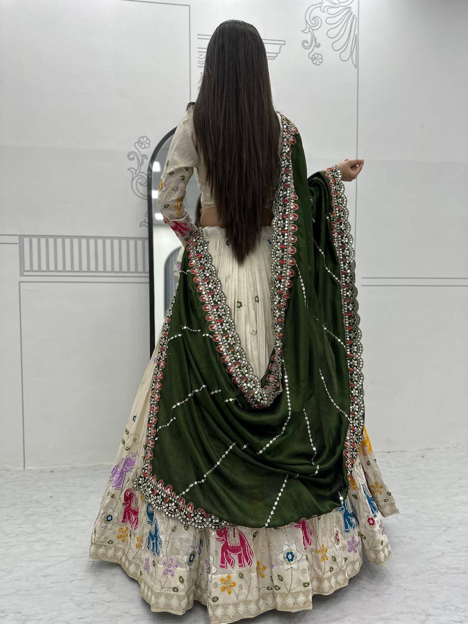 Back view of a woman wearing off-white lehenga choli with olive green dupatta.