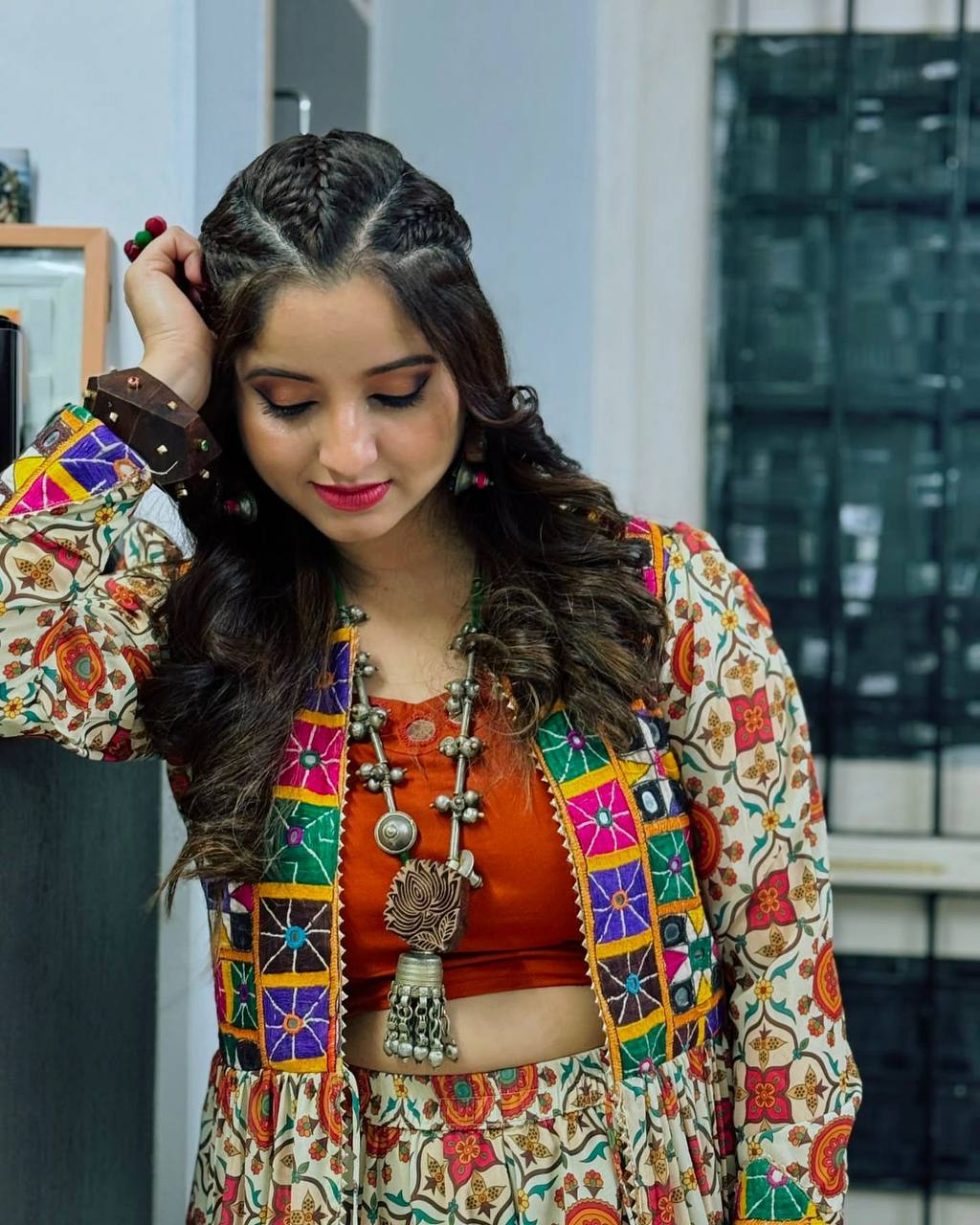 Woman looking down, wearing Kachchi Charm lehenga choli with orange blouse and embroidered mirror work shrug.