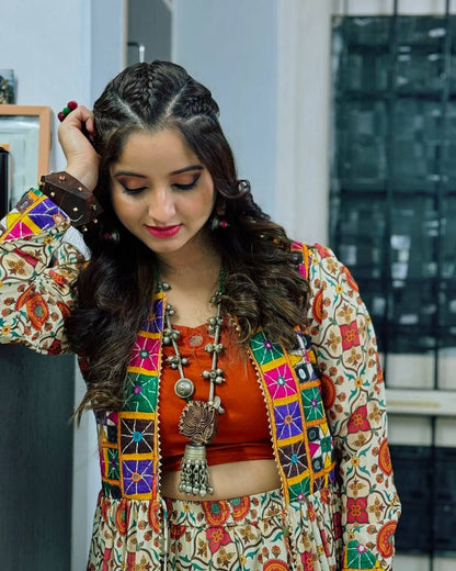 Woman looking down, wearing Kachchi Charm lehenga choli with orange blouse and embroidered mirror work shrug.