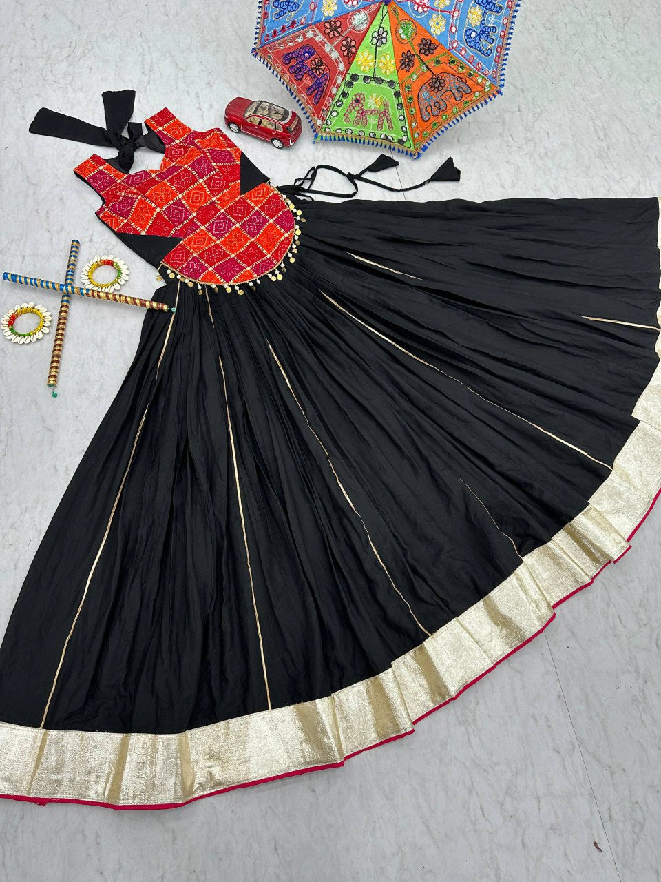 Lehenga choli set displayed with accessories, showing flowing black skirt and festive red choli top.
