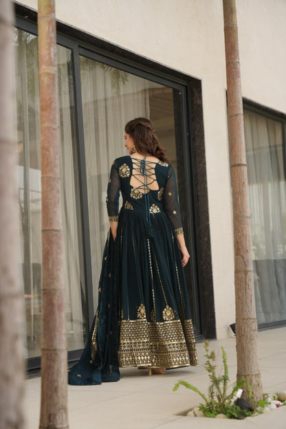 Woman wearing a Rama green gown with zari embroidery, standing by a window.