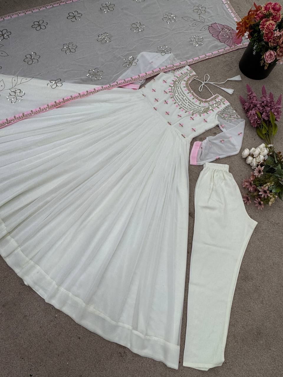 Flatlay of off-white Georgette gown with pink floral embroidered dupatta and matching churidar.