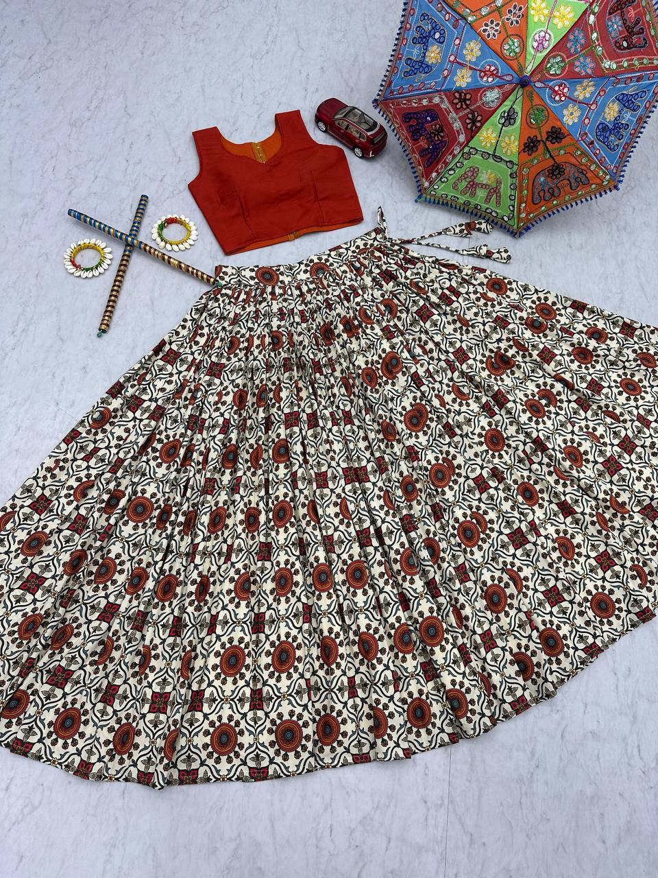 Flat lay of lehenga choli skirt and orange blouse with festive props, highlighting Kachchi embroidery.