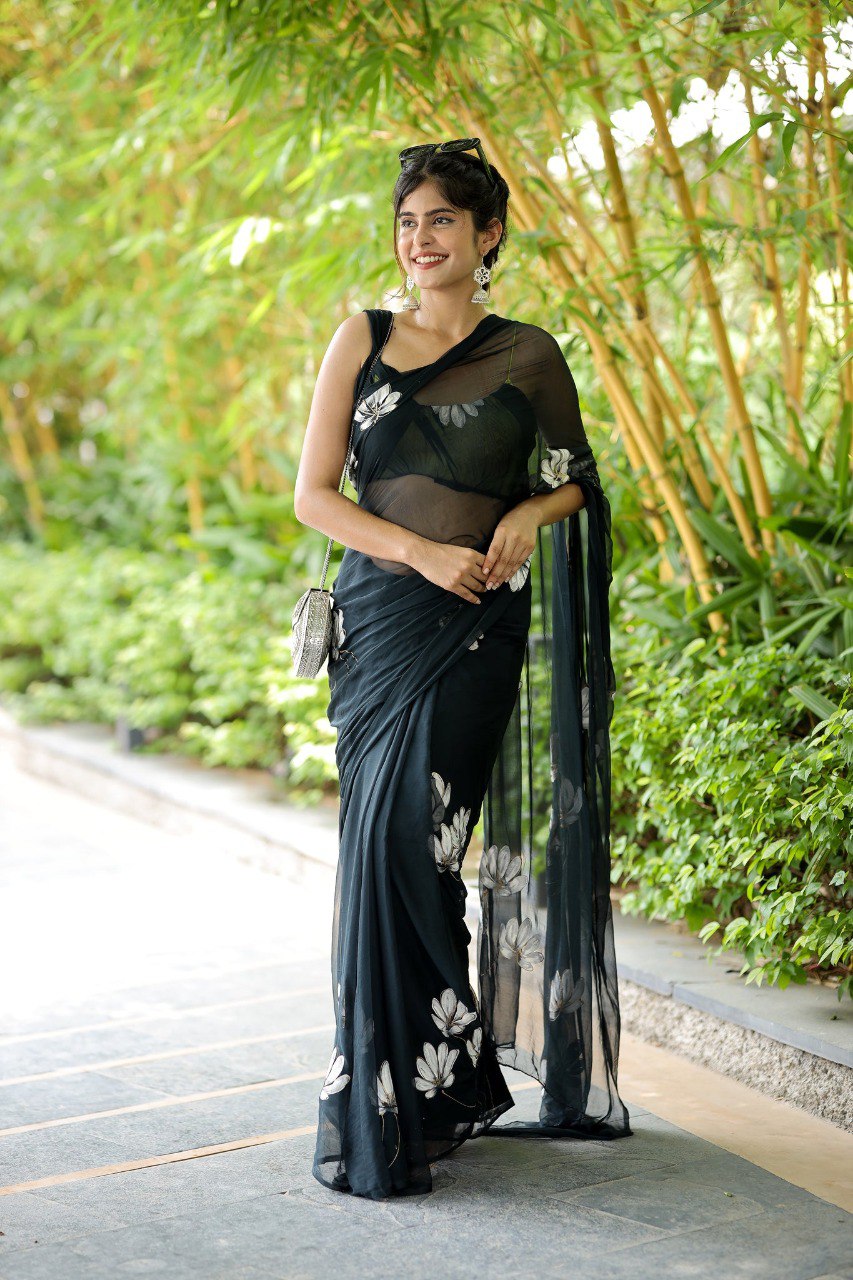Stylish woman in a ready to wear black saree with floral accents and silver purse.