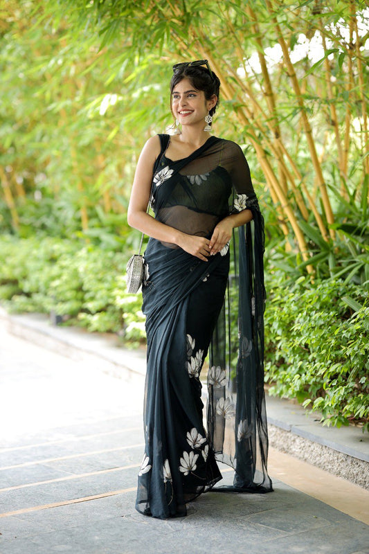 Stylish woman in a ready to wear black saree with floral accents and silver purse.