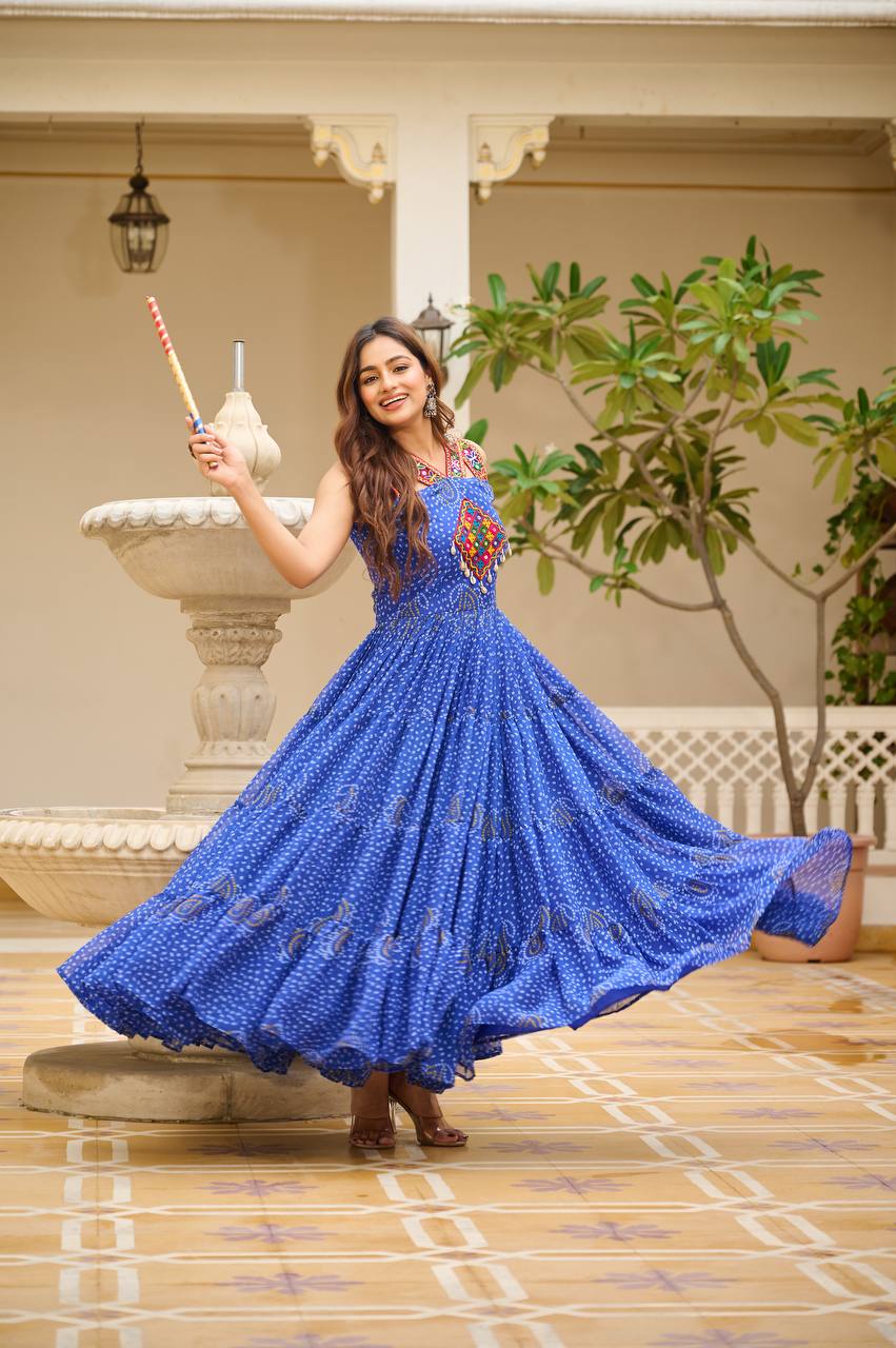 Woman in blue Bandhani Gamathi gown holding dandiya sticks, ready for Navratri dance.