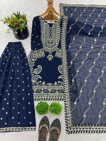 Complete navy blue sharara set with gold embroidery, sheer dupatta, and juttis, displayed on white rug.