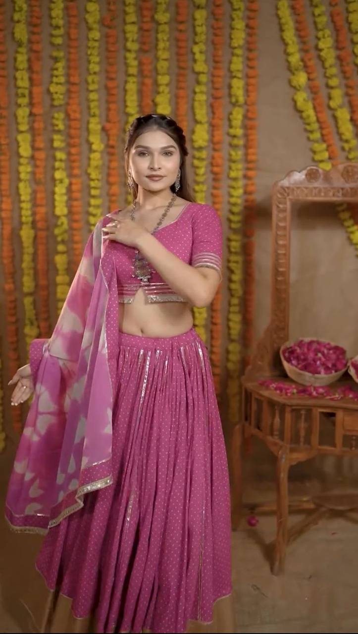 Model poses in a pink cotton lehenga choli set with sweetheart neckline and gold piping dupatta, festive decor.