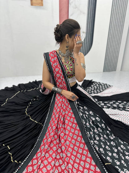 Side view of seated model wearing black, red, and white lehenga with festive dupatta and jewelry.