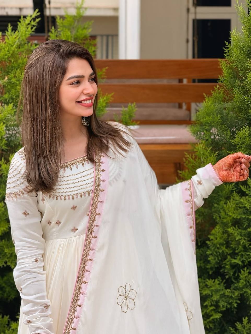 Close-up of off-white gown with gold threadwork and pastel pink border dupatta outdoors.