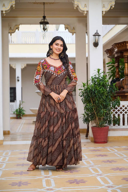Woman in brown Bandhni print Gamathi work gown, featuring vibrant mirror work and full-length style.