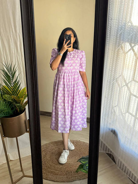 Woman in mirror wearing Ghibli Maxi dress in lilac with white print, paired with white sneakers.