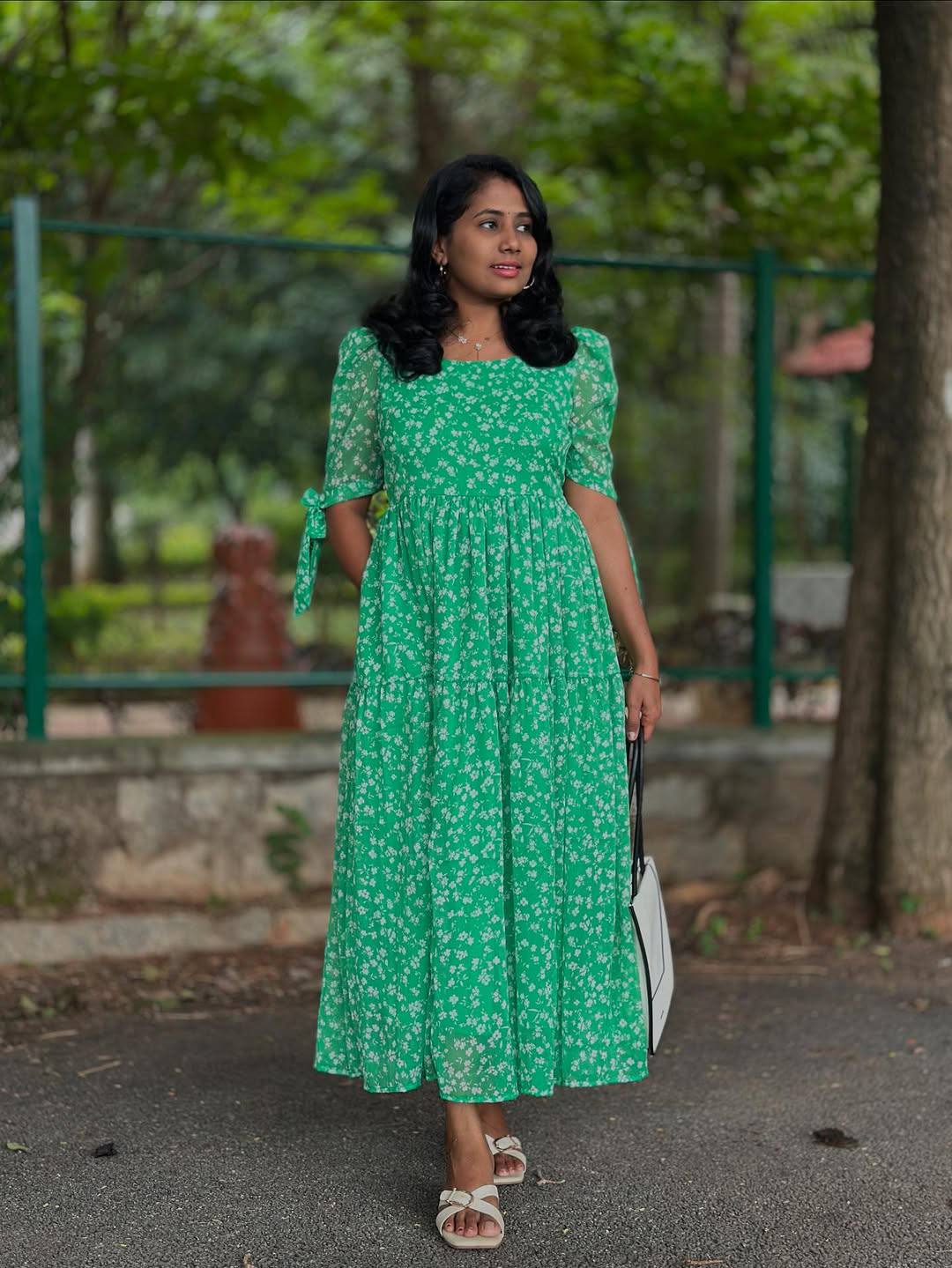 Woman in a green floral georgette maxi dress with tie sleeves holding a tote bag.