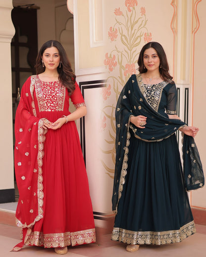 Two women in traditional red and blue dresses with intricate designs, standing indoors.