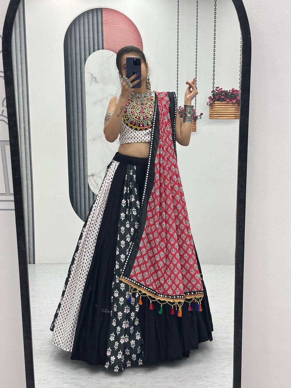 Mirror view of black, white, and red Gujarati lehenga choli set with festive tassel dupatta.