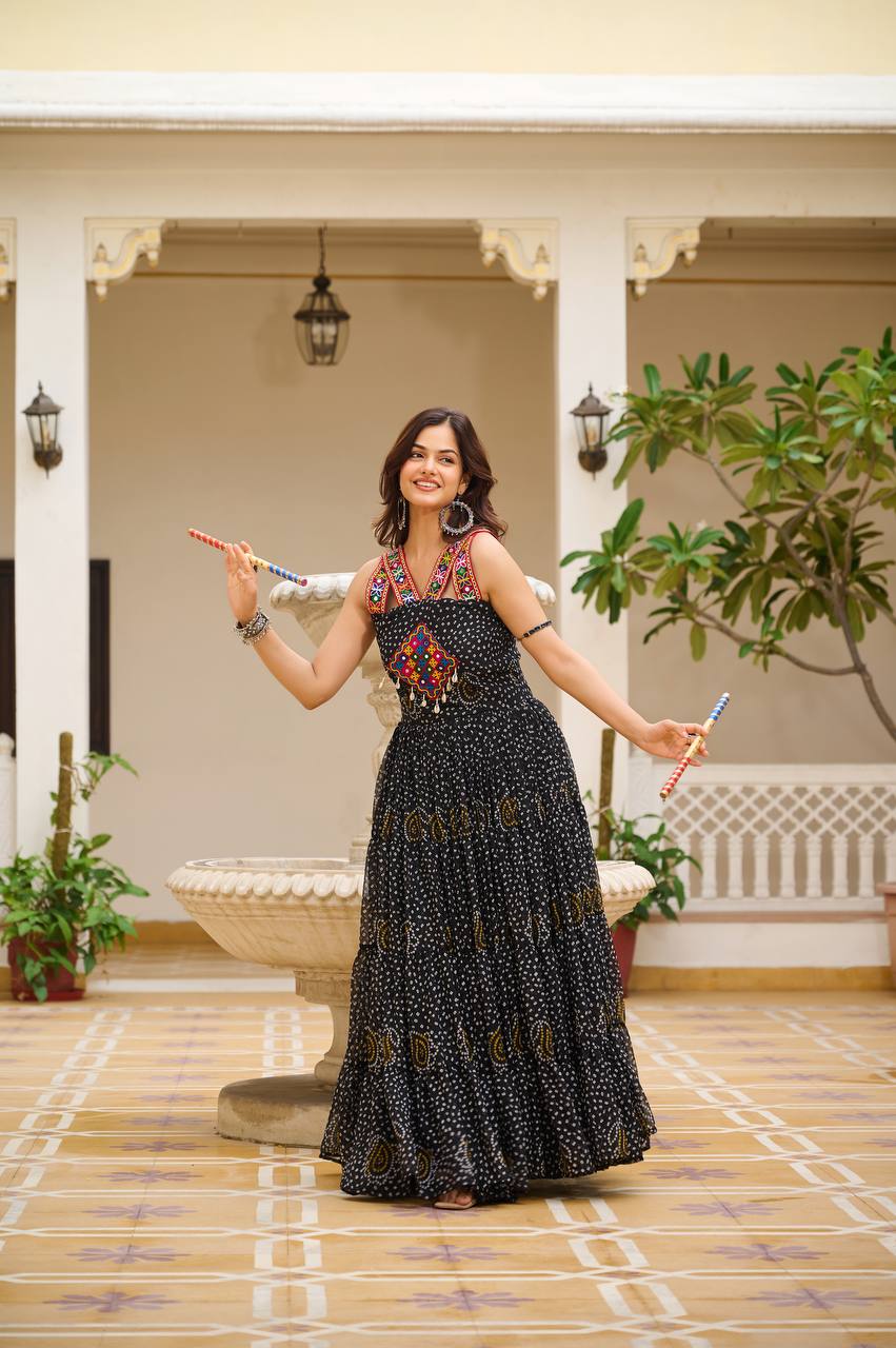 Woman in black Bandhani gown holding dandiya sticks, featuring mirror and codi accents.