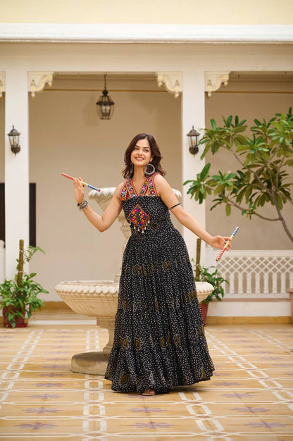 Woman in black Bandhani gown holding dandiya sticks, featuring mirror and codi accents.