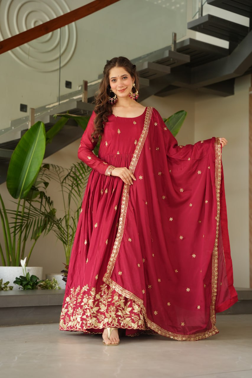 Woman in a red traditional outfit with gold embroidery standing indoors.