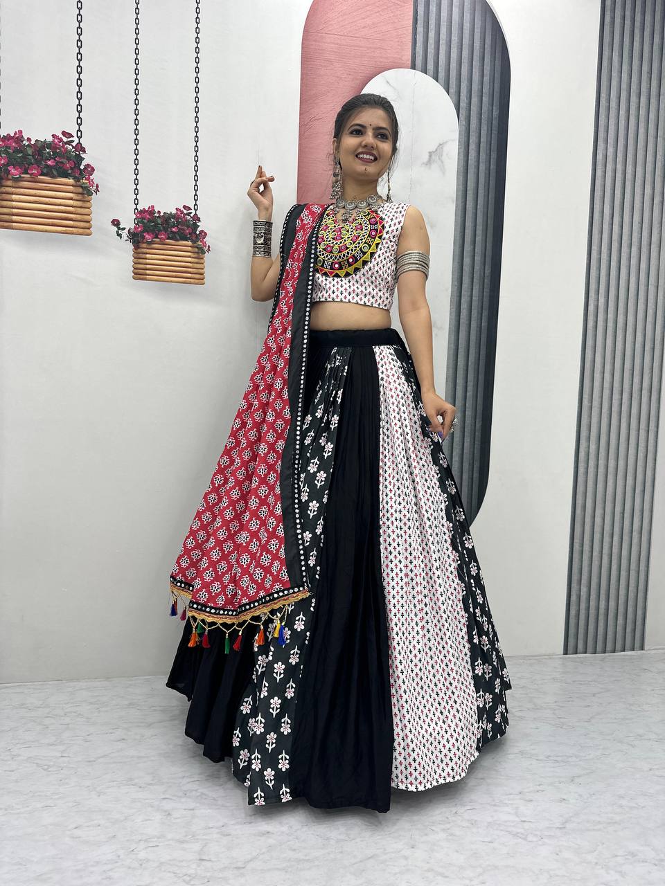 Woman wearing black, red, and white folk print lehenga choli, red dupatta, and silver jewelry.