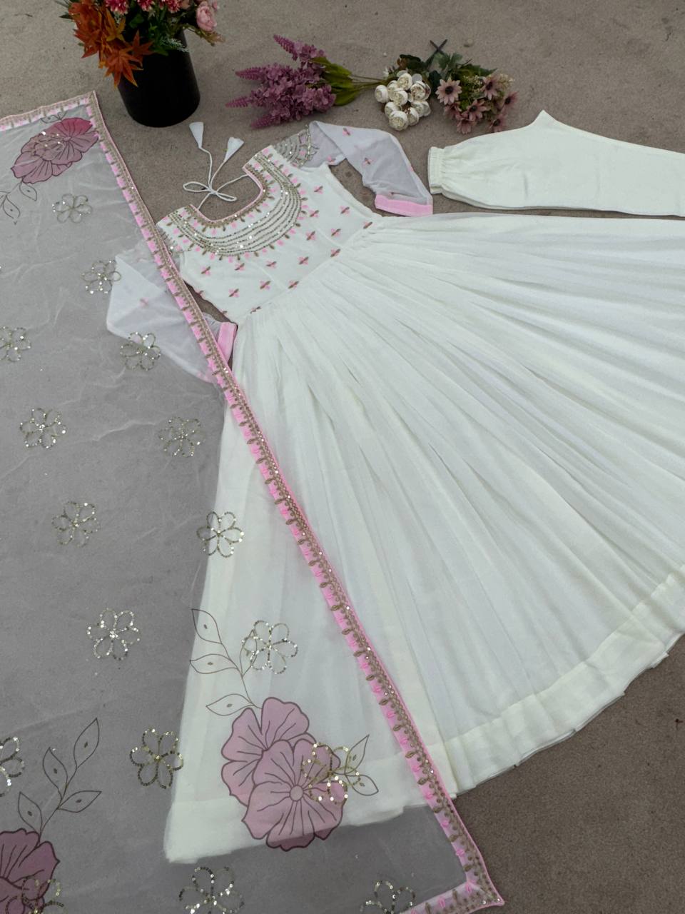 Embroidered off-white party gown set with floral dupatta and churidar, laid out with flowers.